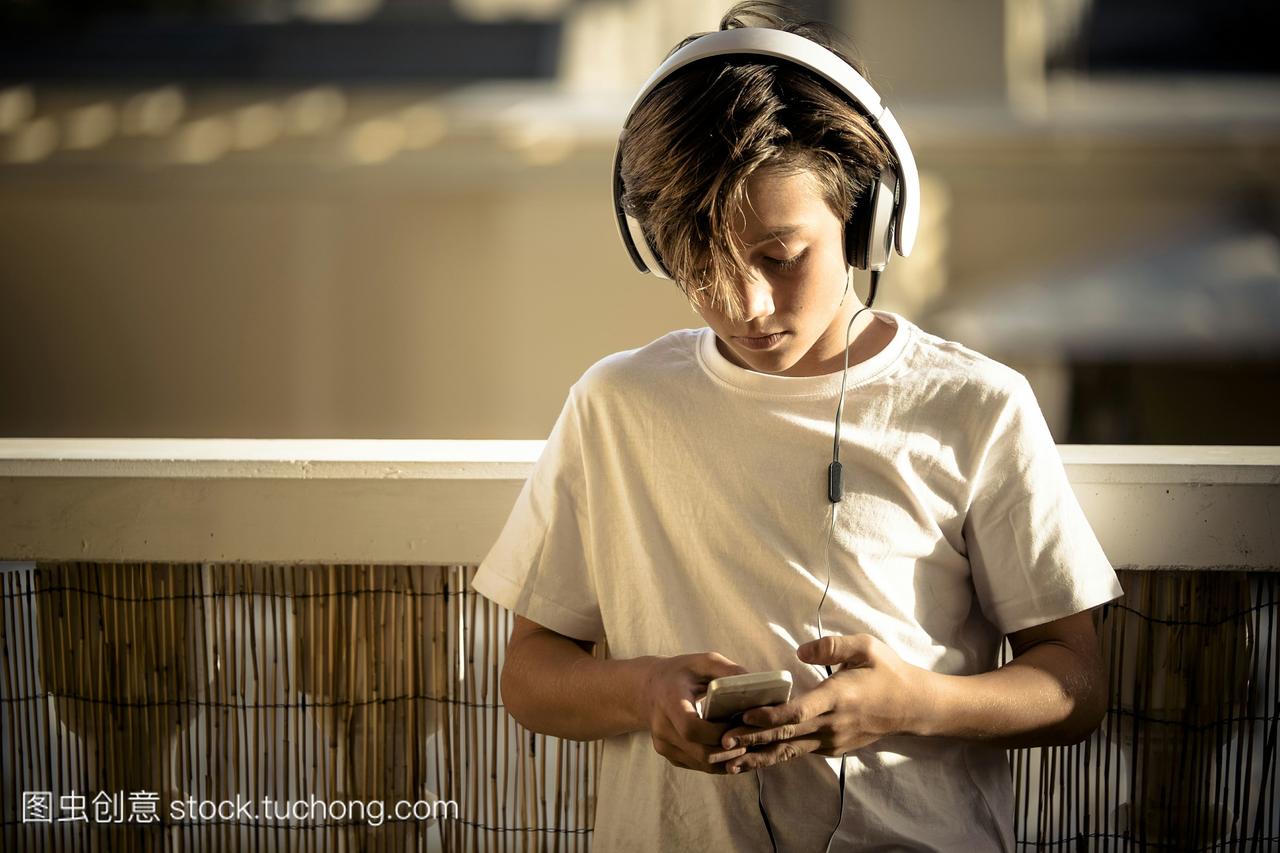 男孩在阳台上用耳机和智能手机听音乐
