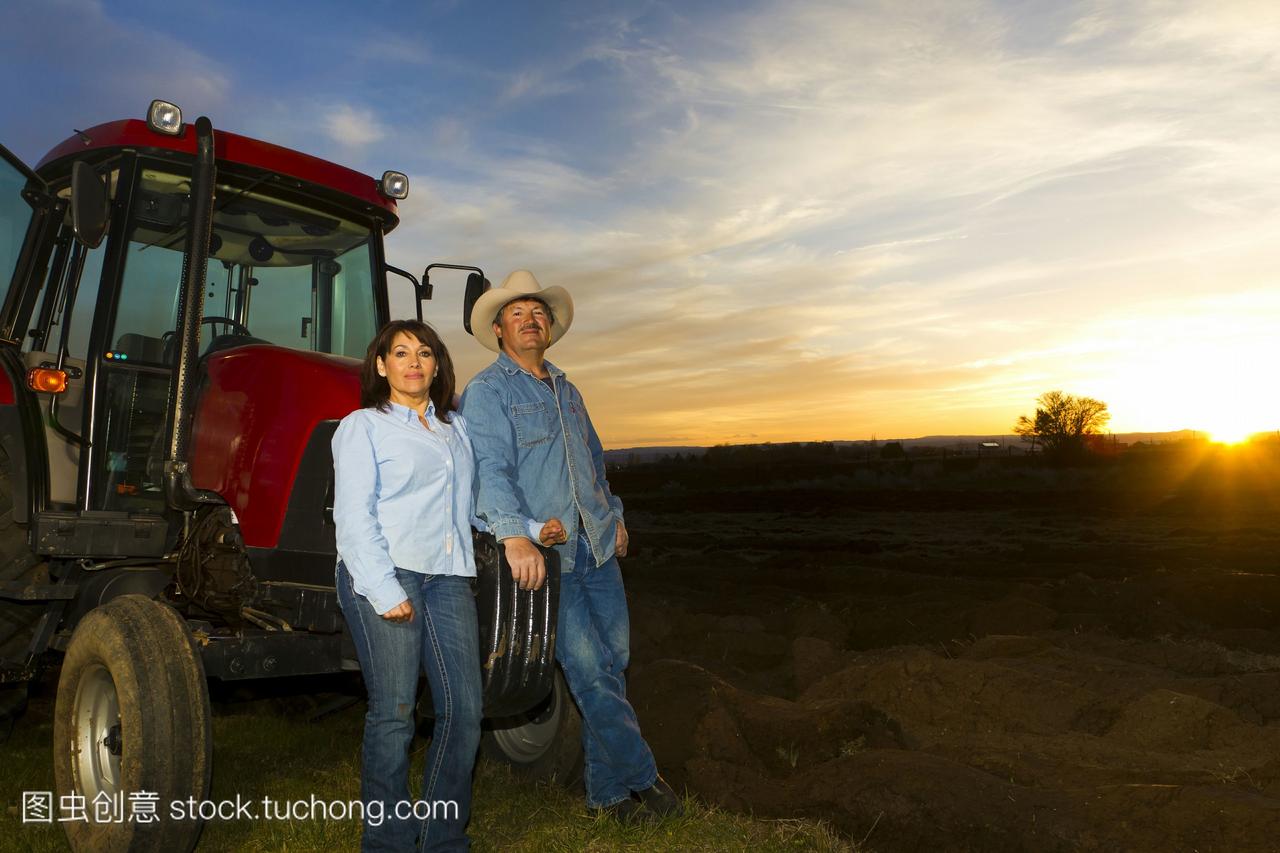 西班牙夫妇站在拖拉机附近的农场上