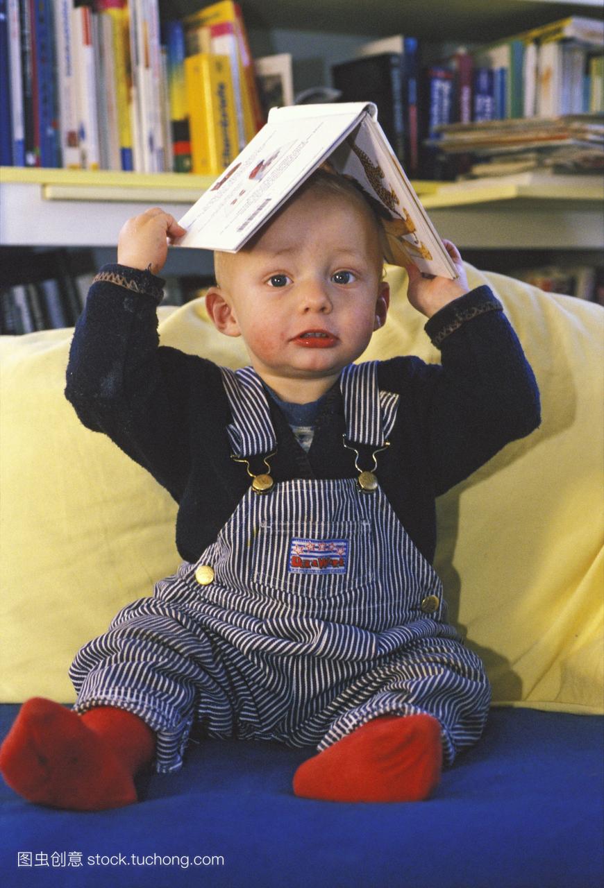 一岁的男孩拿着书像帽子一样