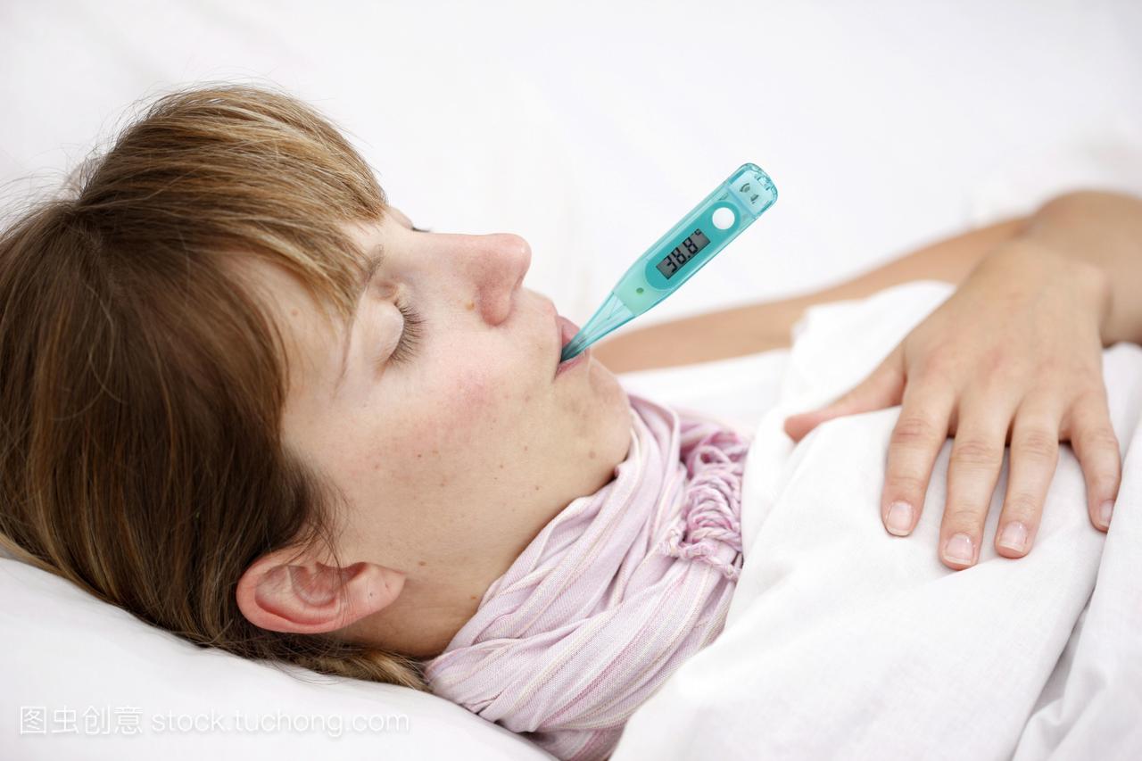 年轻的女人,在床上发烧,用数字温度计测量体温