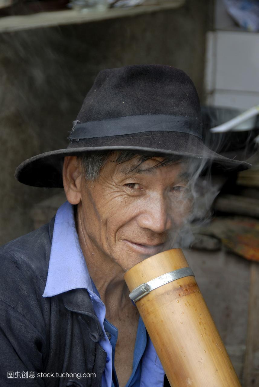 肖像民族学哈尼族的民族的人戴着帽子抽烟吸烟