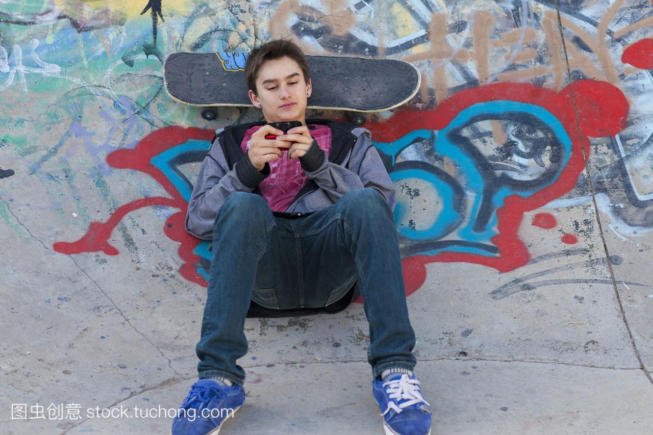 混合种族男孩用手机玩滑板短信