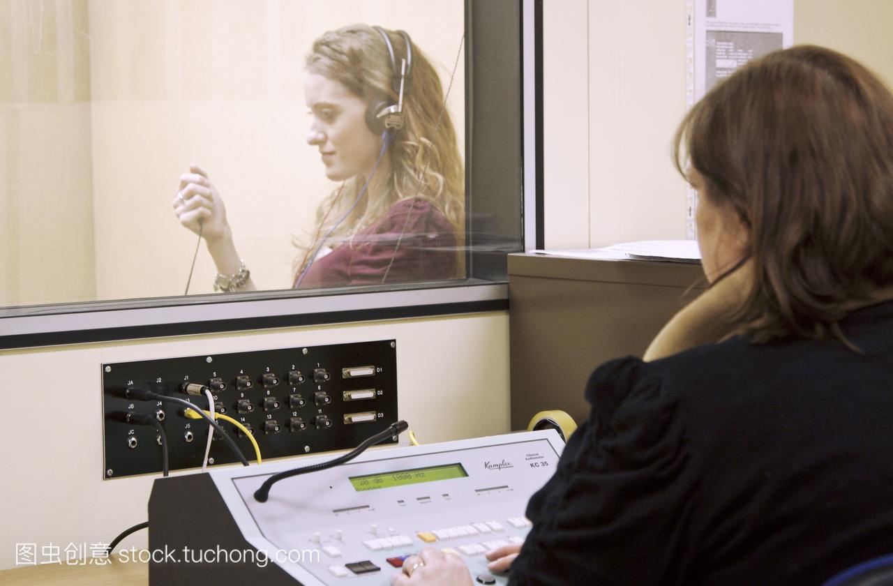 人患者在隔音室玻璃屏风后进行听力听力测试。
