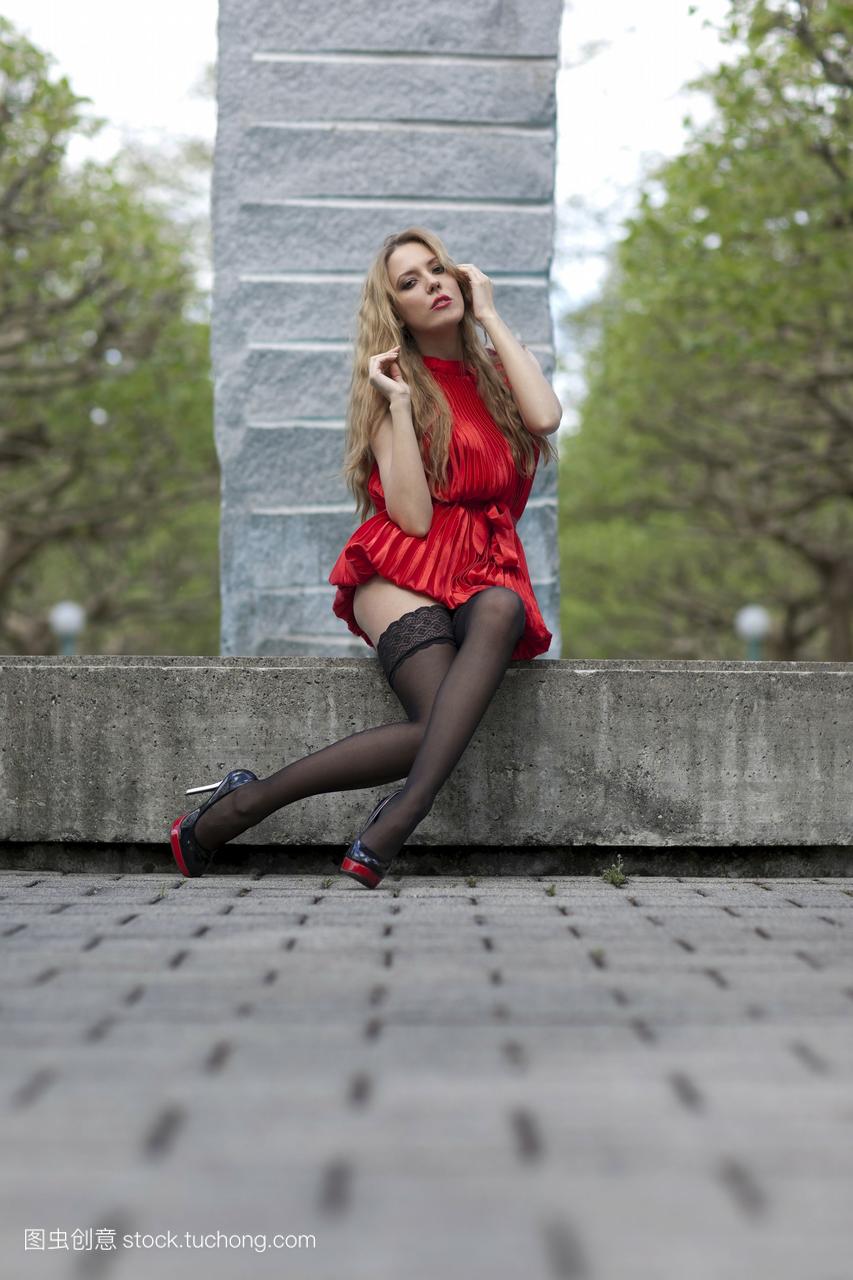 身着红色短裙,黑色长筒袜,高跟鞋坐在喷泉旁的