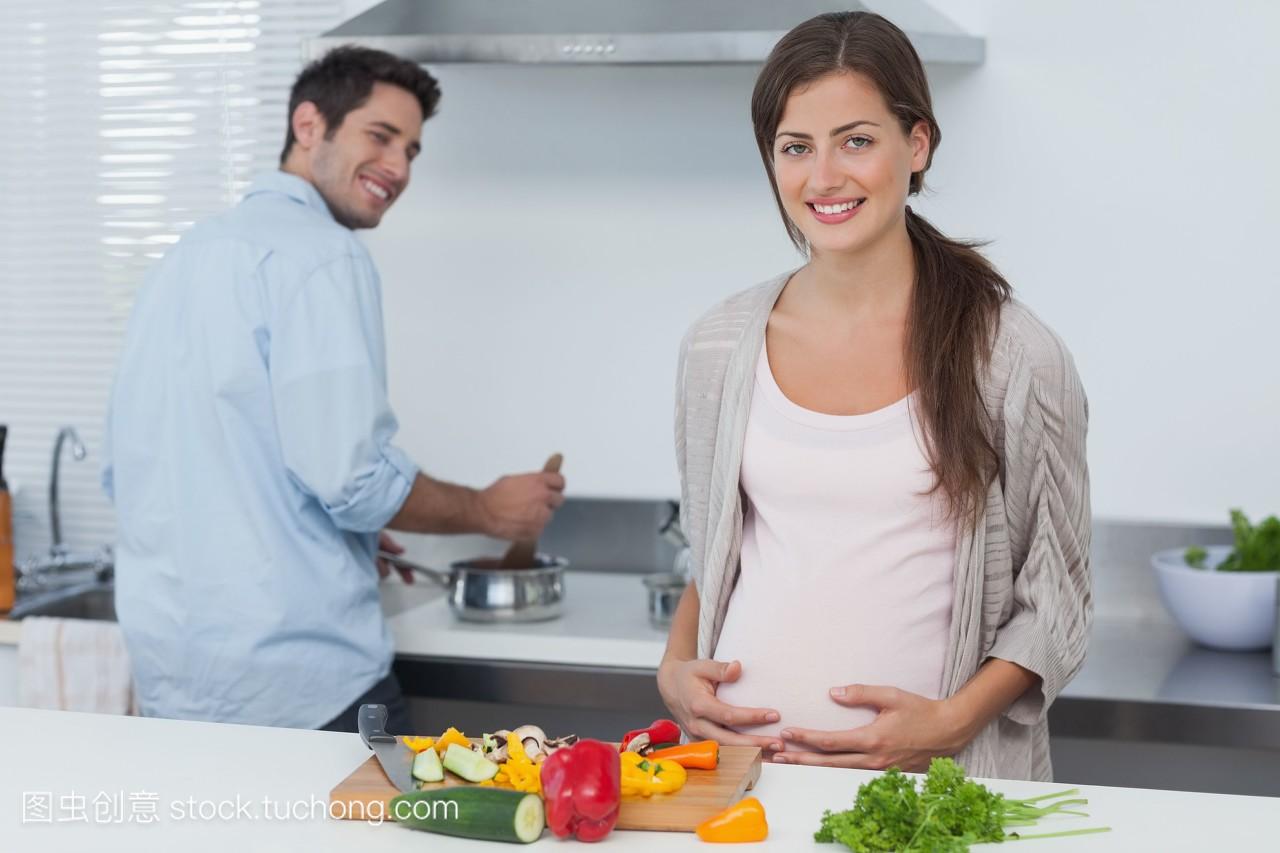 快乐的怀孕妇女抱着她的肚子在厨房和她的丈夫