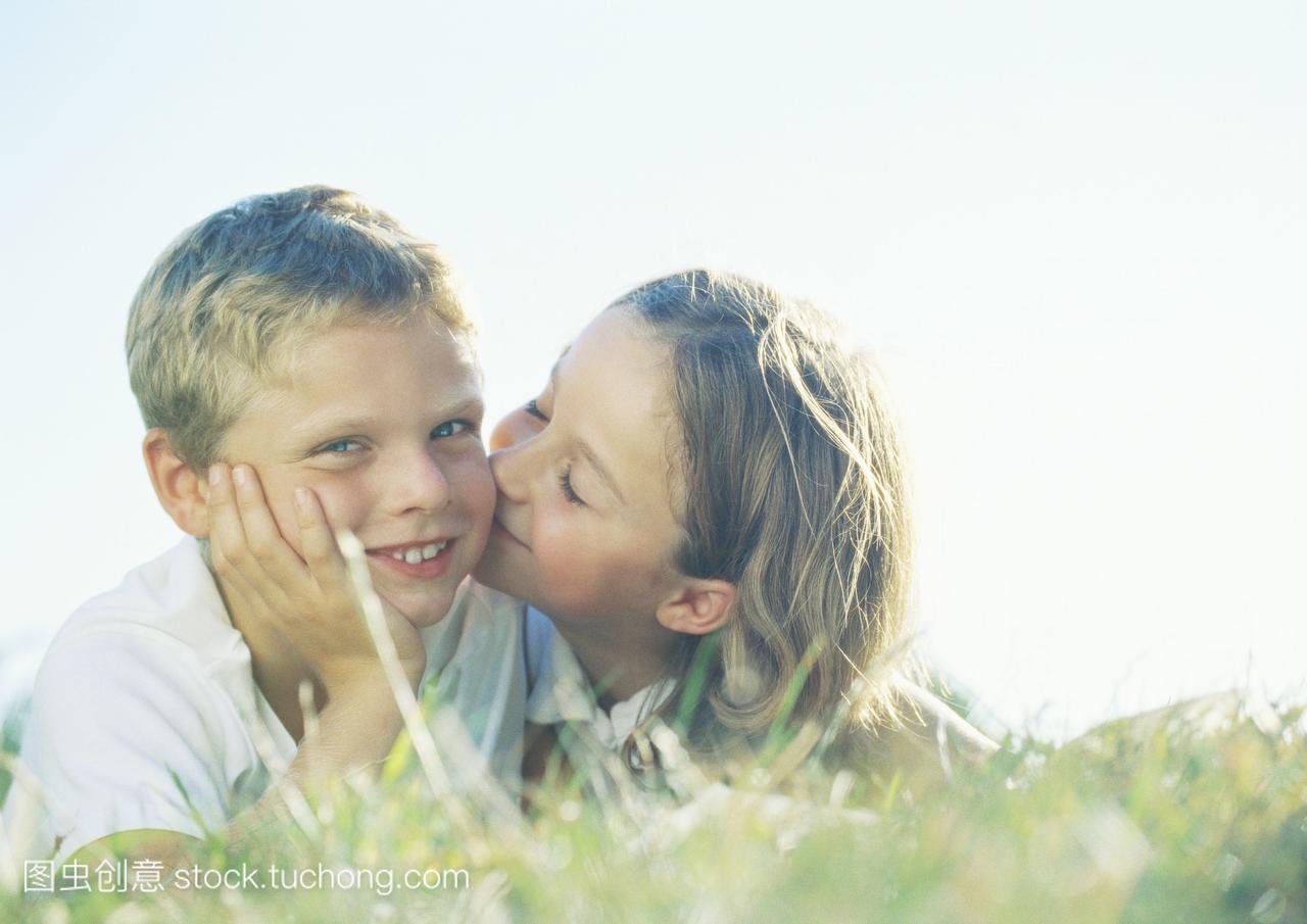 男孩和女孩躺在草地上,女孩亲吻男孩的脸颊