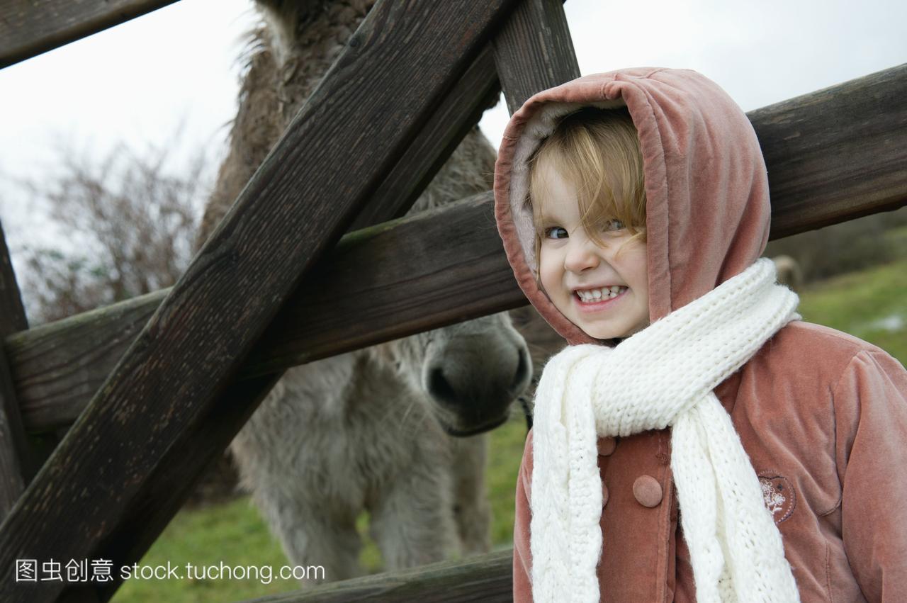 小女孩摆姿势拍着照片,身后有驴子的栅栏,画像