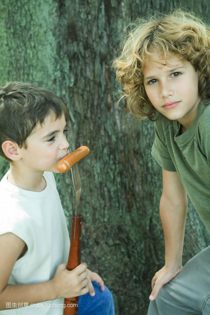 两个男孩,一个吃着叉子吃热狗