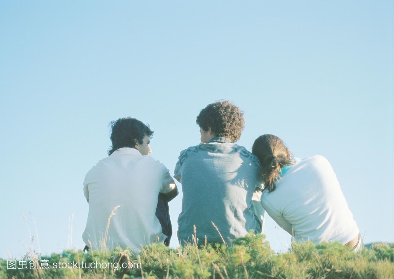三个少年坐在草地上,女孩把头靠在男孩的肩上