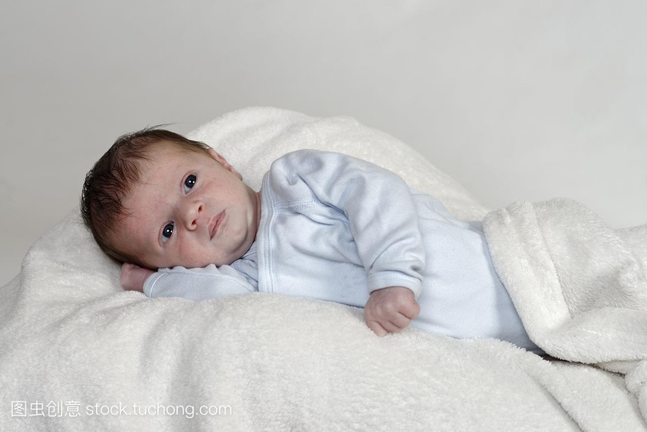 三周大的小男孩躺在白色的毛毯上