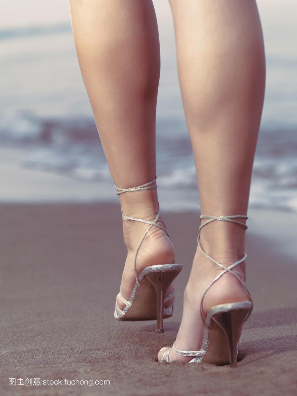 女人穿着高跟鞋在沙滩上行走