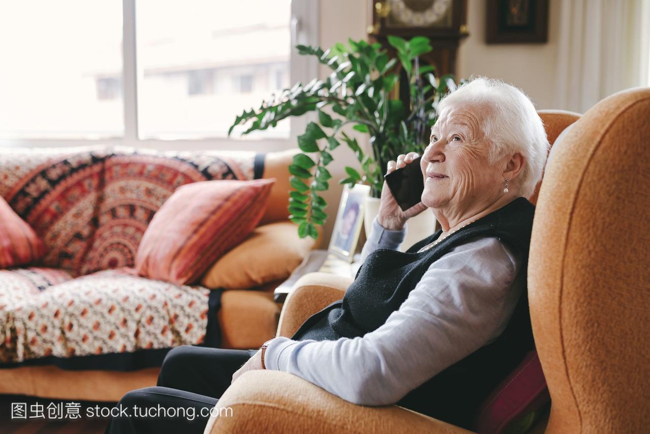 微笑的老年妇女在家里用智能手机打电话