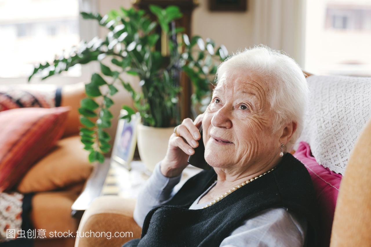 微笑的老年妇女在家里用智能手机打电话