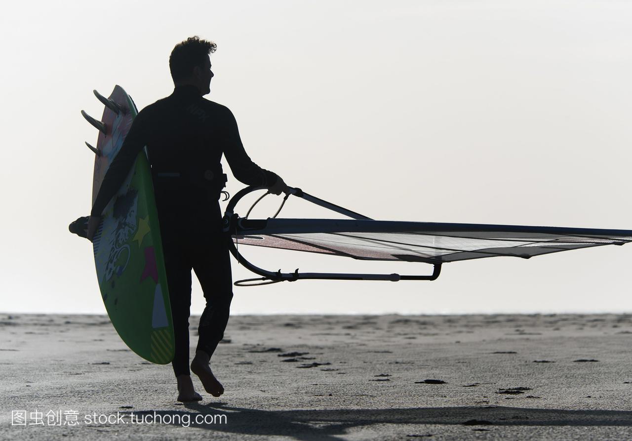 一个人带着风筝冲浪板在沙滩上行走;诺尔安达